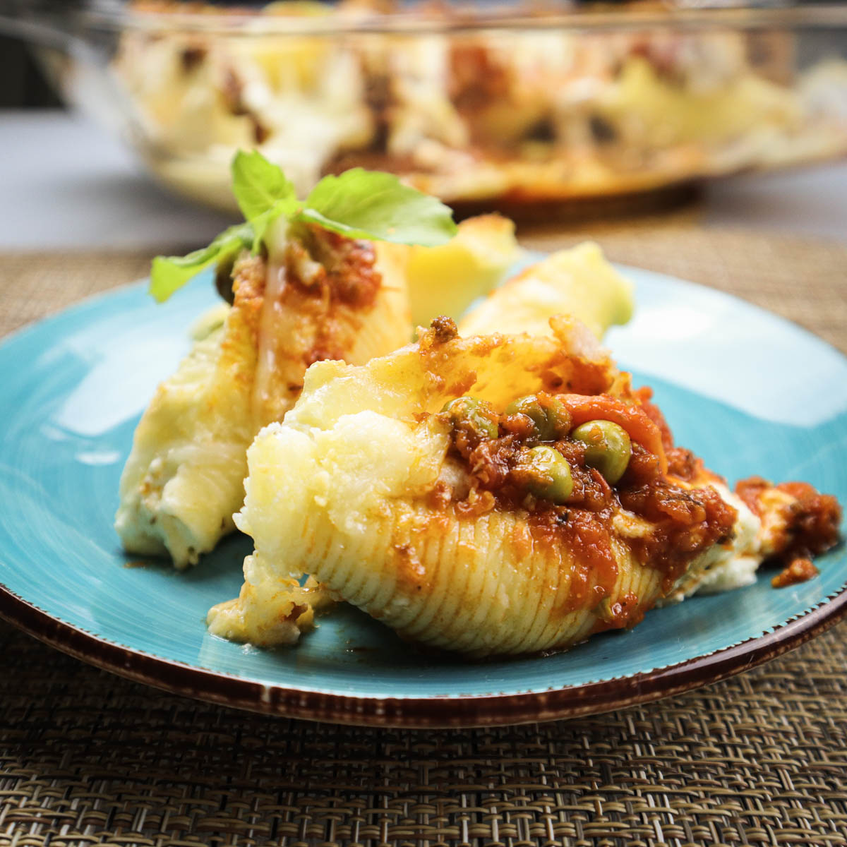 Conchiglioni ripieni al forno presentati su un piatto blue con sullo sfondo la pirofila da forno.